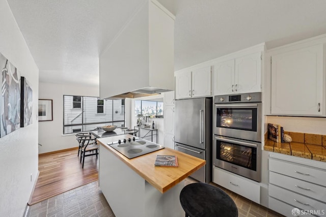 kitchen featuring a textured ceiling, white cabinets, stainless steel appliances, and extractor fan