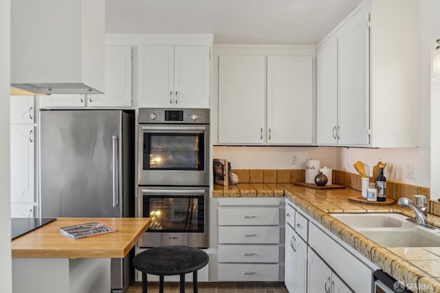 kitchen featuring stainless steel appliances, tile countertops, white cabinets, and sink