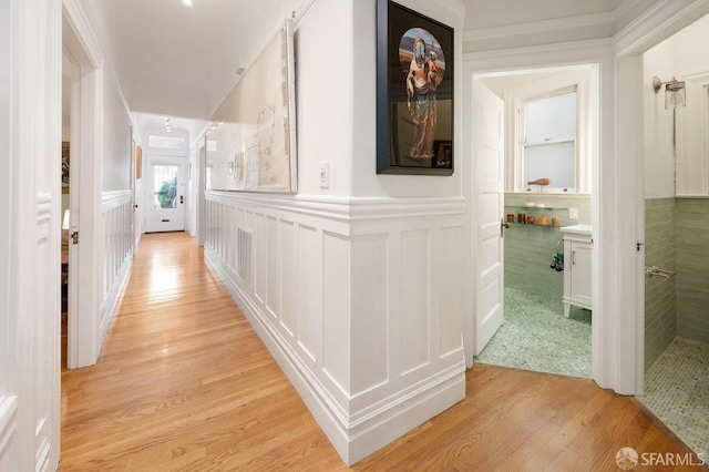 corridor featuring light wood finished floors, wainscoting, and a decorative wall