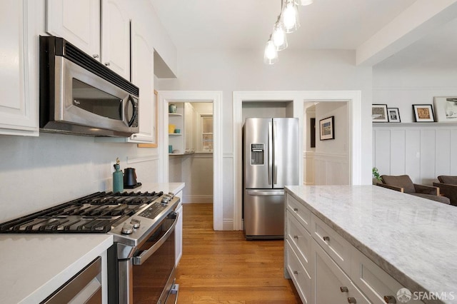 kitchen featuring stainless steel appliances, light wood-type flooring, decorative light fixtures, and white cabinetry