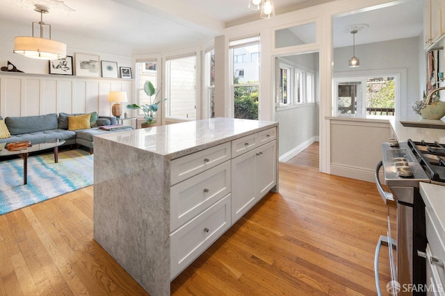 kitchen featuring light stone counters, pendant lighting, stainless steel gas stove, white cabinetry, and light wood-type flooring