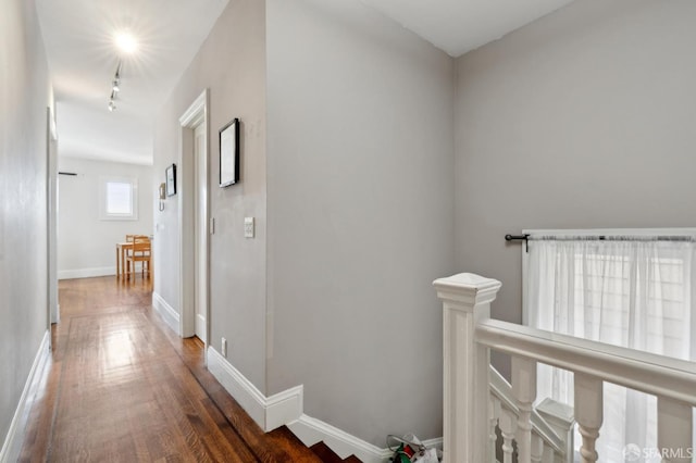 hallway with rail lighting, baseboards, an upstairs landing, and wood finished floors