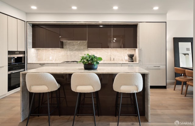 kitchen with a kitchen island, light stone countertops, tasteful backsplash, a breakfast bar, and light hardwood / wood-style floors