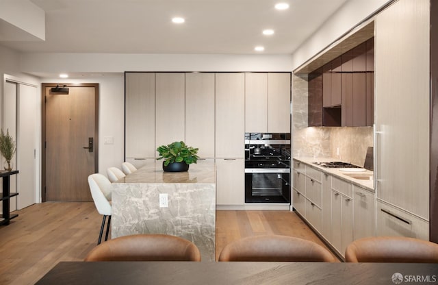 kitchen featuring light hardwood / wood-style flooring, black oven, gas stovetop, light stone countertops, and backsplash