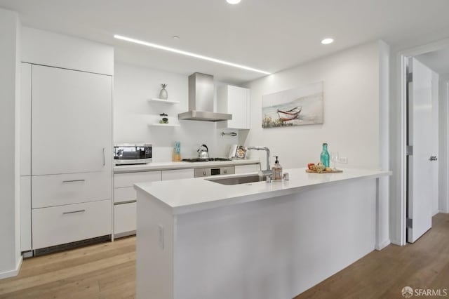 kitchen with wall chimney exhaust hood, modern cabinets, stainless steel microwave, white cabinetry, and a sink