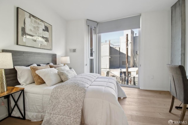 bedroom featuring access to exterior, floor to ceiling windows, visible vents, wood finished floors, and baseboards