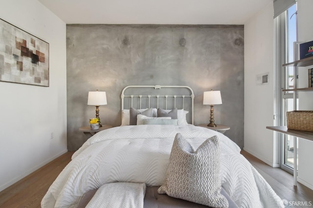 bedroom featuring an accent wall, baseboards, and wood finished floors