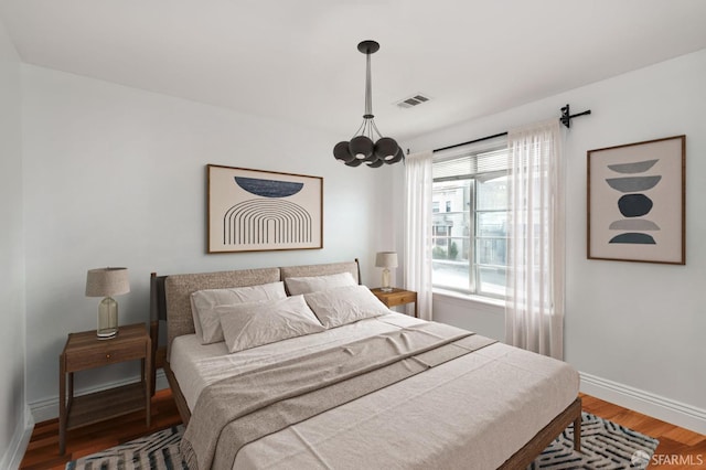 bedroom with visible vents, baseboards, an inviting chandelier, and wood finished floors