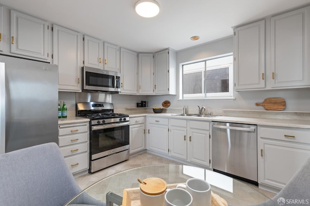 kitchen featuring appliances with stainless steel finishes, white cabinetry, light countertops, and a sink