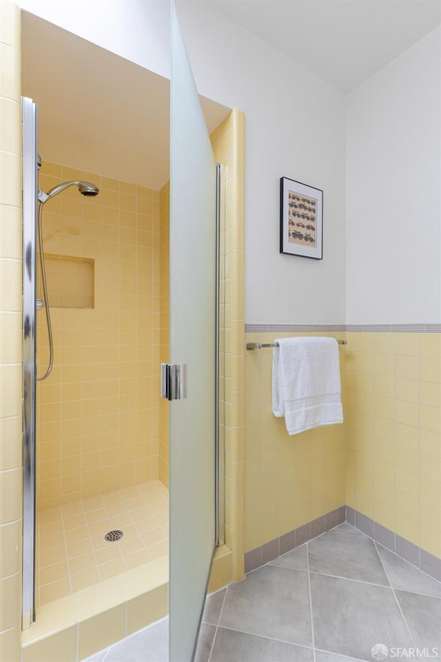 bathroom with tile patterned floors, a stall shower, a wainscoted wall, and tile walls