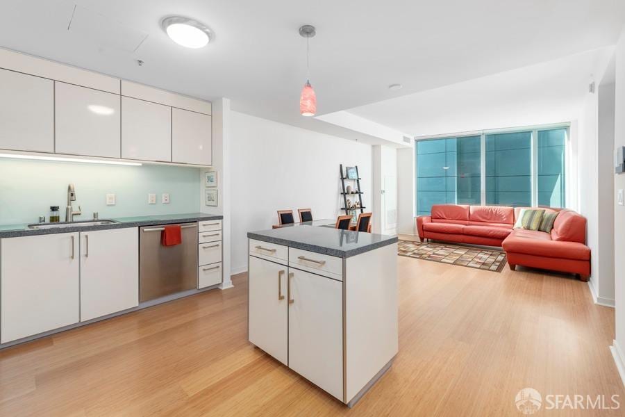 kitchen featuring light hardwood / wood-style floors, stainless steel dishwasher, white cabinets, sink, and pendant lighting