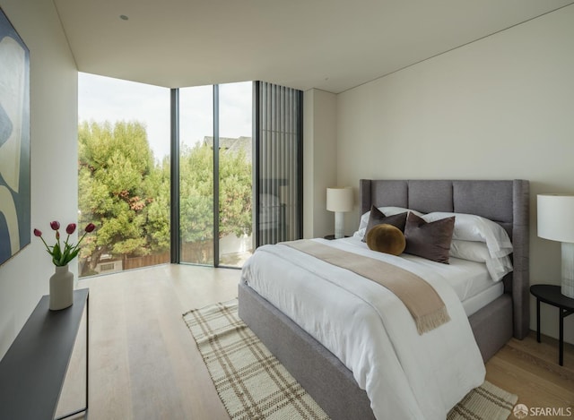 bedroom with light hardwood / wood-style floors, access to exterior, and a wall of windows