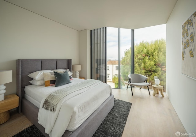 bedroom with multiple windows, access to exterior, wood-type flooring, and a wall of windows