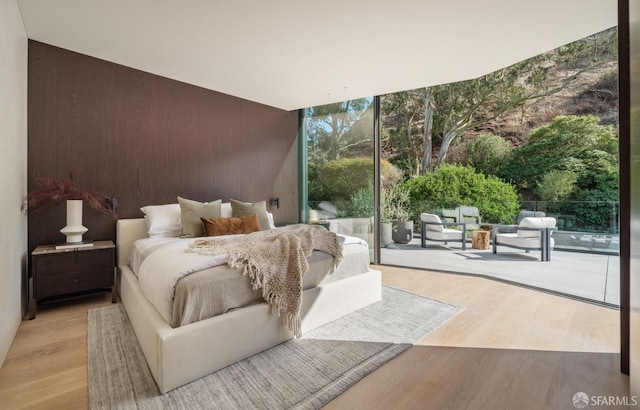 bedroom featuring access to exterior, light wood-type flooring, and a wall of windows