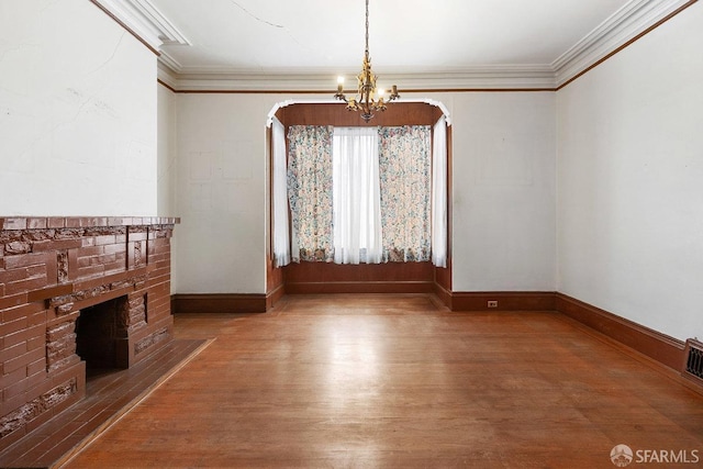 unfurnished living room with crown molding, hardwood / wood-style floors, a brick fireplace, and a notable chandelier