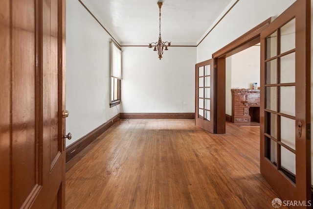 unfurnished room with crown molding, wood-type flooring, a chandelier, and french doors