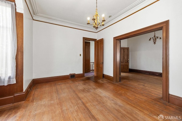 empty room featuring an inviting chandelier, crown molding, and hardwood / wood-style floors