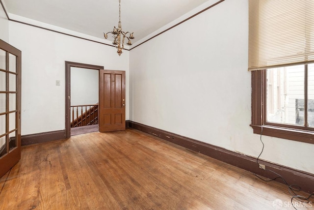 spare room featuring ornamental molding, wood-type flooring, and a chandelier