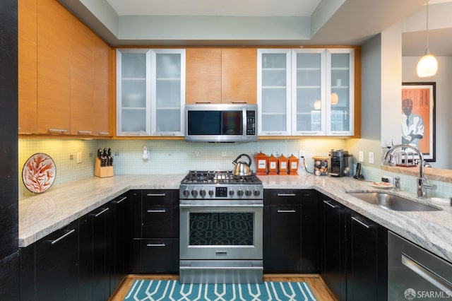 kitchen featuring a sink, light stone counters, backsplash, and appliances with stainless steel finishes