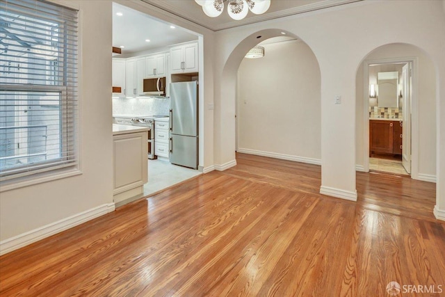 3675 Fillmore St Unit 102, San Francisco, CA 94123 - unfurnished living room featuring arched walkways, healthy amount of natural light, light wood-type flooring, baseboards, and ornamental molding