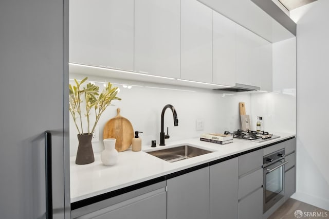 kitchen with stainless steel oven, sink, range hood, white cabinetry, and gas cooktop