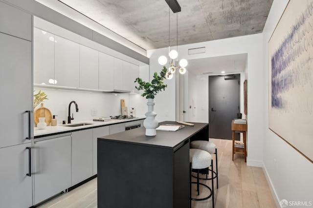 kitchen featuring a center island, sink, light hardwood / wood-style floors, decorative light fixtures, and white cabinets