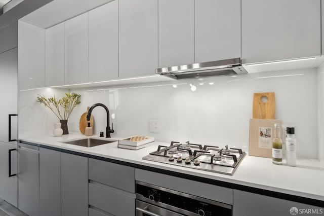 kitchen featuring wall oven, ventilation hood, stainless steel gas cooktop, sink, and white cabinetry