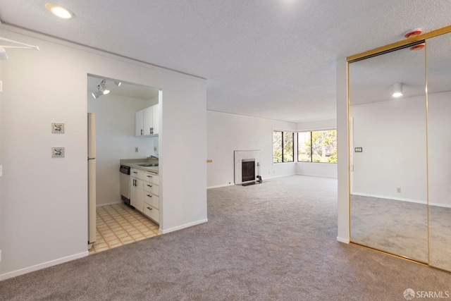 unfurnished living room featuring a textured ceiling, light carpet, a sink, a fireplace with flush hearth, and baseboards