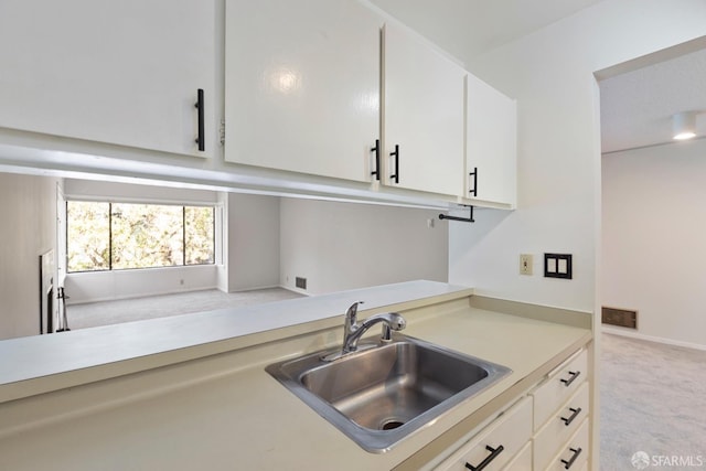 kitchen featuring light carpet, a sink, visible vents, white cabinetry, and light countertops