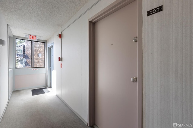 hall with a textured ceiling and light colored carpet