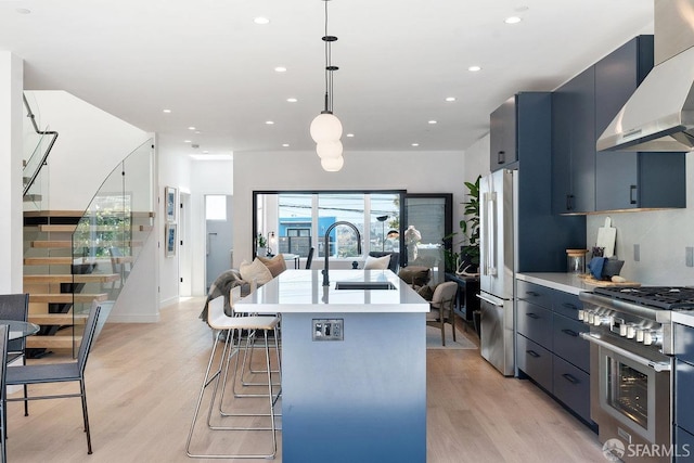 kitchen featuring sink, decorative light fixtures, wall chimney range hood, stainless steel appliances, and light hardwood / wood-style floors