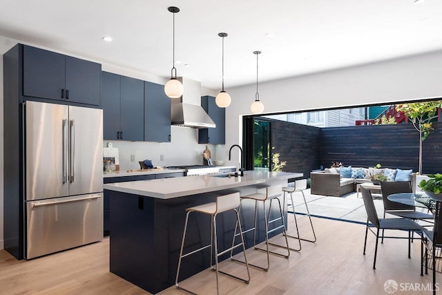 kitchen with light wood-type flooring, an island with sink, a kitchen bar, hanging light fixtures, and stainless steel appliances