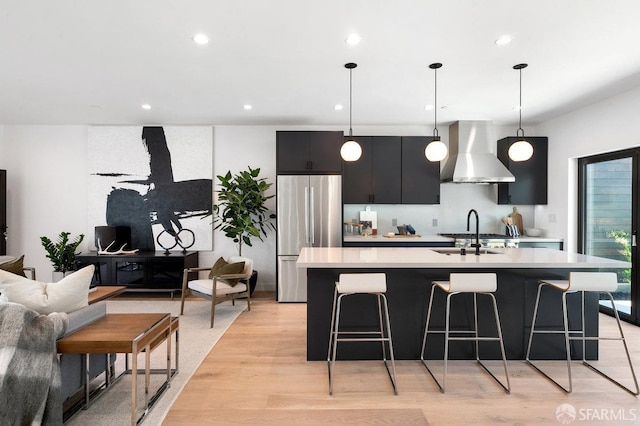 kitchen featuring hanging light fixtures, sink, light hardwood / wood-style flooring, stainless steel refrigerator, and range hood