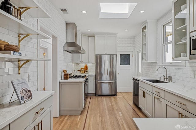 kitchen with sink, a skylight, stainless steel appliances, light stone countertops, and wall chimney range hood