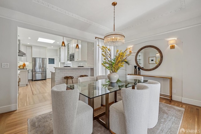 dining room with an inviting chandelier, a skylight, and light hardwood / wood-style floors