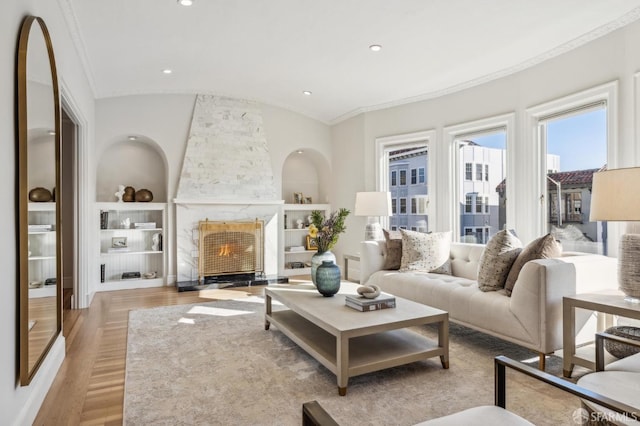 living room featuring vaulted ceiling, ornamental molding, light wood-type flooring, and built in shelves