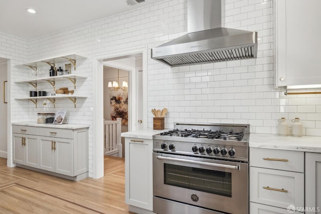 kitchen with high end range, wall chimney range hood, tasteful backsplash, and light hardwood / wood-style floors