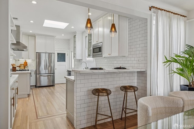 kitchen with wall chimney exhaust hood, a breakfast bar, appliances with stainless steel finishes, kitchen peninsula, and white cabinets