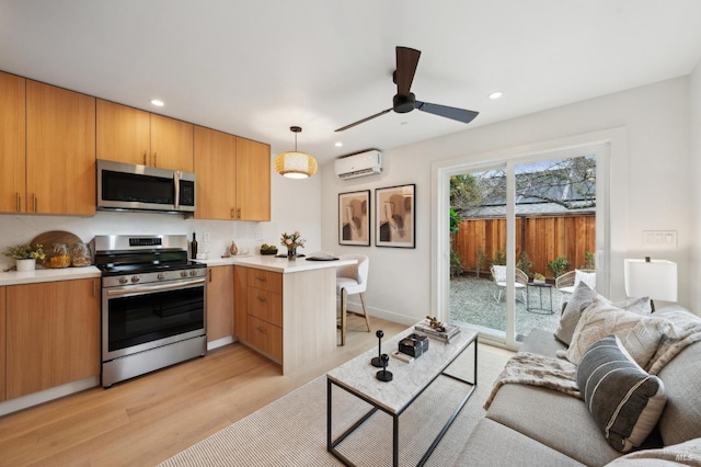 kitchen with appliances with stainless steel finishes, hanging light fixtures, kitchen peninsula, a wall unit AC, and light hardwood / wood-style flooring