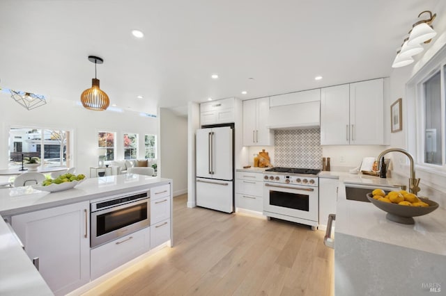 kitchen featuring white appliances, premium range hood, white cabinetry, decorative backsplash, and sink