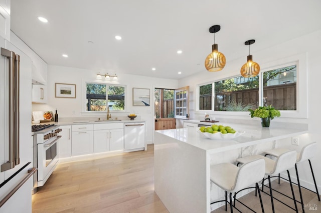 kitchen with hanging light fixtures, sink, white cabinets, white appliances, and a kitchen bar