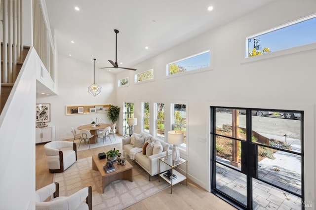 living room with light wood-type flooring, a towering ceiling, and ceiling fan