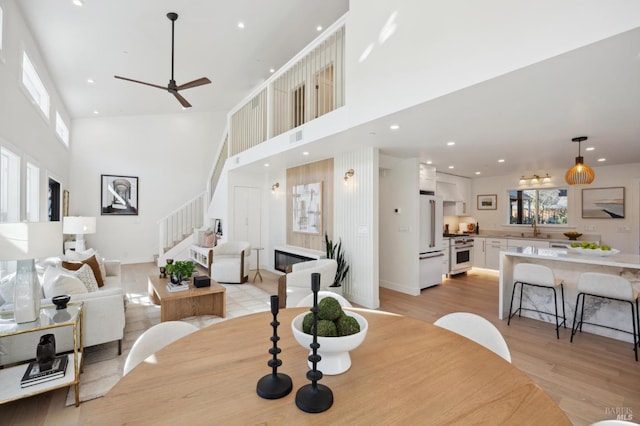 dining space featuring sink, light wood-type flooring, a high ceiling, and ceiling fan