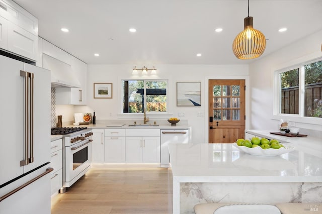 kitchen featuring pendant lighting, white cabinetry, high end appliances, light hardwood / wood-style floors, and sink