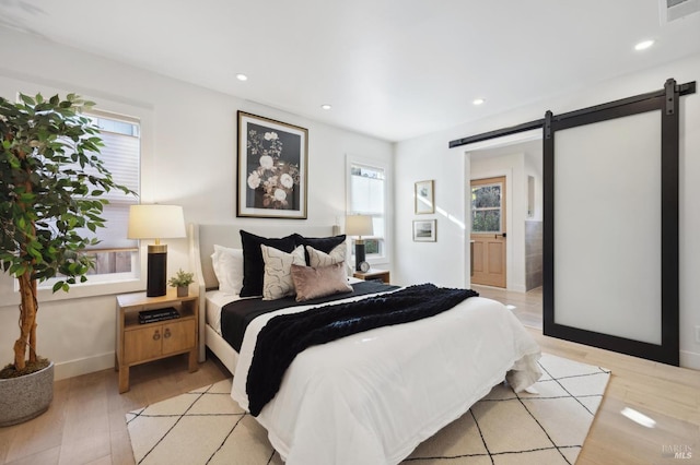 bedroom with multiple windows, ensuite bathroom, a barn door, and light wood-type flooring