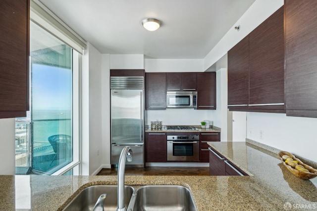 kitchen with a wealth of natural light, appliances with stainless steel finishes, light stone counters, and a sink