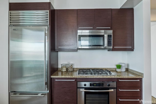 kitchen with dark brown cabinets, stainless steel appliances, and light stone countertops