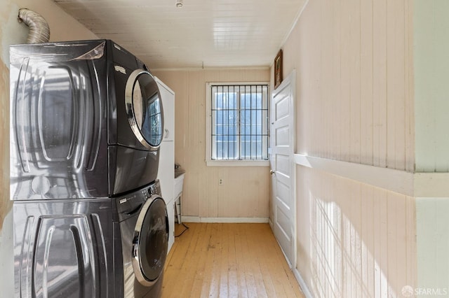 laundry area featuring light hardwood / wood-style floors, wood walls, and stacked washing maching and dryer