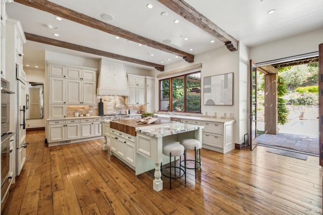 324 Palm Ave, Kentfield, CA 94904 - kitchen featuring a breakfast bar area, light wood-style flooring, beamed ceiling, decorative backsplash, and custom exhaust hood