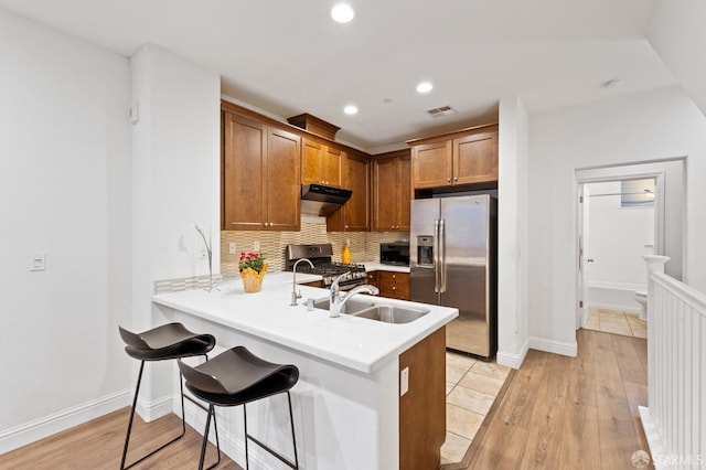 kitchen featuring stainless steel appliances, light wood-type flooring, decorative backsplash, a breakfast bar area, and kitchen peninsula